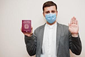 homme européen en tenue de soirée et masque facial, montre le passeport italien avec la main du panneau d'arrêt. verrouillage du coronavirus dans le concept de pays d'europe. photo