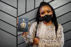 une femme afro-américaine portant un masque facial noir montre un passeport jamaïcain en main. coronavirus dans le pays américain, fermeture des frontières et quarantaine, concept d'épidémie de virus. photo