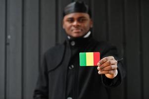 l'homme africain porte du durag noir tient le drapeau du mali à la main isolé sur fond sombre. photo