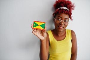 femme afro-américaine aux cheveux afro, porter un singulet jaune et des lunettes, tenir le drapeau de la grenade isolé sur fond blanc. photo