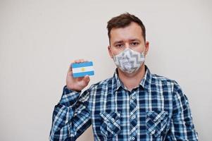 homme en chemise à carreaux montre la carte du drapeau argentin à la main, portez un masque de protection isolé sur fond blanc. concept de coronavirus des pays américains. photo