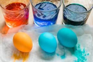 processus de mort des oeufs de pâques. tasses en verre transparent avec de l'eau colorée et des œufs colorés, vue de dessus photo