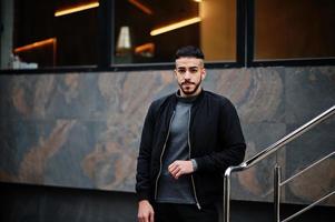 portrait d'un homme à la barbe arabe élégant portant un col roulé gris et un jaket noir. mec modèle arabe. photo