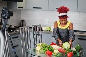 femme afro-américaine filmant son blog diffusé sur des aliments sains dans la cuisine à domicile. elle coupe le chou. photo