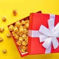 boîte-cadeau rouge avec un arc blanc plein de savoureux pop-corn au caramel sur fond jaune.
