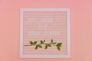 carte de lettrage avec citation rester à la maison et boire du café décoré d'une branche de printemps avec des feuilles fraîches vertes. fond de motivation de printemps. photo
