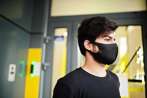 urbain jeune hipster indien portant tout le stand noir près de l'entrée du code. un gars sud-asiatique cool avec un masque de protection du visage, pendant la nouvelle normalité. photo