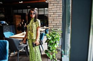 une femme afro-américaine glamour porte une robe de serpent à la mode et des lunettes de soleil pose au restaurant. photo