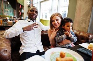 une famille multiethnique heureuse avec un garçon passe du temps au restaurant. relations de l'homme africain et de la femme européenne blanche. photo