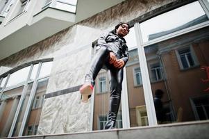 belle femme afro-américaine à la mode posant dans une veste et un pantalon en cuir noir dans la rue. photo