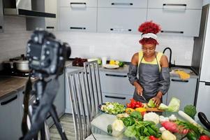 femme afro-américaine filmant son blog diffusé sur des aliments sains dans la cuisine à domicile. elle coupe le chou. photo