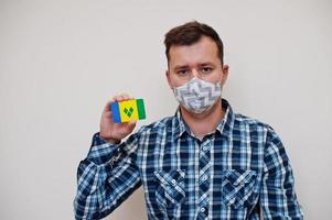 homme en chemise à carreaux montre saint vincent et la carte du drapeau des grenadines à la main, portez un masque de protection isolé sur fond blanc. concept de coronavirus des pays américains. photo