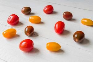 tomates cerises rouges, vertes et jaunes éparpillées sur une table en bois. lumière naturelle. photo