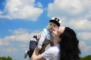 heureuse jeune fille, maman joue avec son bébé dans ses bras sur fond de ciel bleu avec des nuages. espace de copie. photo