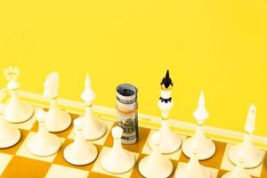 gros plan de billets de cent dollars nous roulés debout sur un échiquier au lieu d'une pièce d'échecs. fond jaune. espace de copie. photo