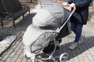 fête des mères. jeune femme marchant dans le parc du printemps avec landau. mère passe du temps avec son enfant à l'extérieur photo