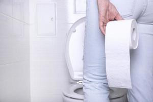 femme qui pisse souffrant de diarrhée dans des toilettes blanches, dans des toilettes avec un rouleau de papier blanc à la main. photo