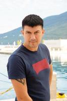homme caucasien dans un t-shirt bleu pose près d'un yacht dans le port, tivat, monténégro. photo