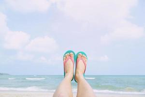 les jeunes portent les chaussures sandales gros plan montrent les pieds se détendre sur la plage sur le sable en profitant du soleil frais le jour d'été ensoleillé. profiter de la mer photo
