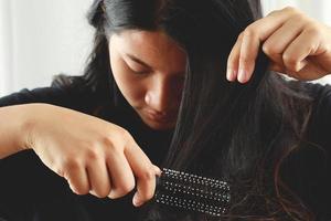 vue arrière jeune femme inquiète du problème de perte de cheveux, du déséquilibre hormonal, du concept de stress. beaucoup de cheveux tombent après avoir peigné la brosse à cheveux à la main. femme démêlé ses cheveux avec un peigne, soins de santé photo