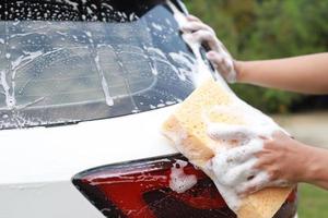 personnes travailleur homme tenant la main éponge jaune et fenêtre nettoyante en mousse à bulles pour laver la voiture. concept de lavage de voiture propre. laisser de la place pour écrire des messages. photo