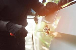 gros plan main de voleur de voiture tenant un tournevis inviolable et un gant noir volant une automobile essayant la poignée de porte pour voir si le véhicule est déverrouillé en essayant de pénétrer à l'intérieur. photo