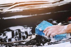 personnes travailleur homme tenant la main éponge bleue et fenêtre nettoyante en mousse à bulles pour laver la voiture. concept de lavage de voiture propre. laisser de la place pour écrire des messages. photo