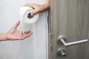 l'homme souffre de diarrhée main tenir le rouleau de papier de soie devant la cuvette des toilettes. constipation dans la salle de bain. traitement des douleurs à l'estomac et de l'hygiène, concept de soins de santé. photo