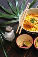 recette de khao soi, khao soi, khao soi kai, nouilles thaïlandaises khao soi, curry de poulet avec assaisonnement servi sur table en bois noir avec feuilles décoratives, photo verticale.
