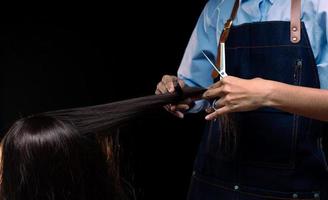 salon de coiffure montre la main avec une coupe de cheveux professionnelle aux ciseaux pour faire la beauté d'une cliente dans un salon de coiffure. peigne de coiffure définir le style de la tête de cheveux longs et couper le travail en tant que coiffeur sur fond noir photo