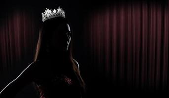 portrait du concours de beauté de miss pageant en robe de soirée à sequins robe longue avec couronne de diamants scintillants, silhouette exposition discrète avec rideau, éclairage de studio fond sombre dramatique photo