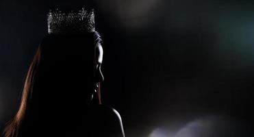 portrait du concours de beauté de miss pageant en robe de soirée à sequins robe longue avec couronne de diamants scintillants, silhouette exposition discrète avec rideau, éclairage de studio fond sombre dramatique photo