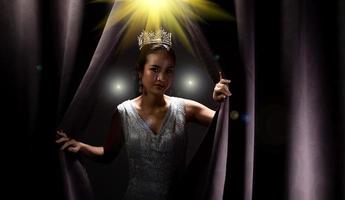 le concours de beauté miss pageant porte une longue robe de soirée à sequins avec une couronne de diamants scintillants, une femme asiatique ouvre le rideau violet après avoir remporté le tour final comme une nouvelle façon de vivre, opportunité, changement, isolé photo