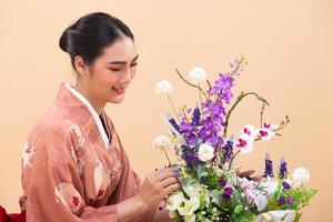 une jeune femme japonaise asiatique de 20 ans porte un kimono traditionnel, fait un arrangement floral d'ikebana photo