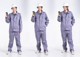 pleine longueur 20s jeune femme électricienne ingénieur de course mixte, utilisant un téléphone portable Internet, porte un uniforme gris. femme entrepreneur se sent sourire heureux sur fond blanc isolé photo