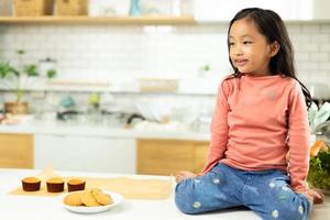 une personne d'âge préscolaire fait la cuisine de gâteaux dans la cuisine, une jeune fille prépare une décoration jolie avec plaisir éduque sur le cupcake pour l'anniversaire de sa soeur. désordre de crème sur le visage et la bouche des cheveux bouclés, se sentir heureux, espace de copie photo