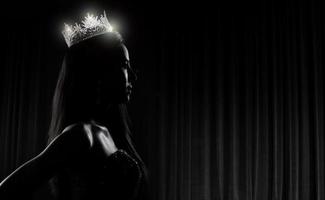 portrait du concours de beauté de miss pageant en robe de soirée à sequins robe longue avec couronne de diamants scintillants, silhouette exposition discrète avec rideau, éclairage de studio fond sombre dramatique photo