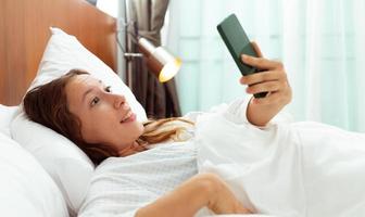 une femme caucasienne dort sur l'oreiller du lit et l'alarme de réveil du téléphone. les femmes se sentent somnolentes et choquées lorsqu'elles décrochent un smartphone et regardent l'heure de travailler le matin à l'aube. jeune adulte exprime un choc, copiez l'espace photo