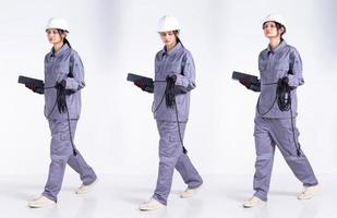 pleine longueur 20s jeune ingénieur de course mixte femme électricienne, marchant vers l'avant gauche droite, porter un uniforme gris. Femme entrepreneur tenir le câble de prise électrique sourire heureux sur fond blanc isolé photo