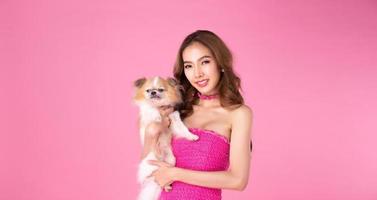 fille porter une robe rose chocky tenir un chien mignon et regarder la caméra sur fond rose photo