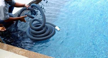 femme ouvrière propre piscine privée avec aspirateur tube bleu chaque semaine en été, piscine de type sel avec océan comme style horizontal avec cocotiers photo