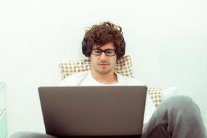 un jeune homme caucasien travaille à domicile sur un ordinateur portable et se connecte en ligne au bureau à l'intérieur pour un lieu de travail Internet à distance. jeune homme adulte est un travail indépendant intelligent sur un ordinateur portable assis sur la chambre à coucher, espace de copie photo