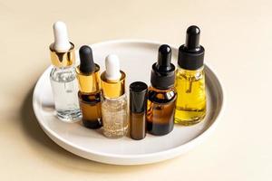 ensemble de différents flacons compte-gouttes avec sérum de soin de beauté, acide hyaluronique et vitamines sur plateau en céramique. cosmétique maison et concept de spa photo