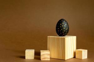 fond de pâques à la mode. des œufs peints en or et en noir se tiennent sur des cubes en bois, des podiums sur fond marron. photo