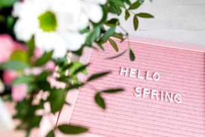 texte bonjour printemps sur le tableau à lettres rose avec de belles fleurs épanouies, composition de style minimalisme, espace de copie pour votre texte. photo