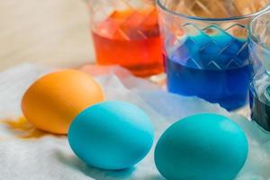 processus de mort des œufs de Pâques. tasses en verre transparent avec de l'eau colorée. oeufs colorés au premier plan photo