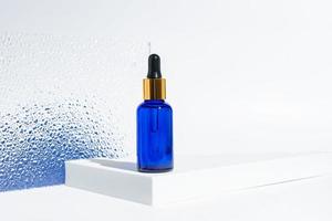 flacon cosmétique en verre bleu avec un compte-gouttes sur fond blanc avec dégradé bleu. concept de cosmétiques naturels, huiles essentielles naturelles et produits de soins de la peau photo