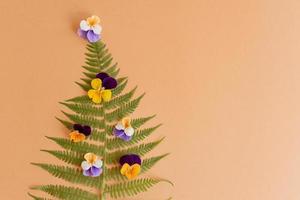 arbre de noël fait de feuilles de fougère et de pensées sur fond beige avec espace de copie. notion de nouvel an photo