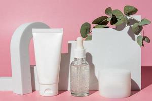 bouteilles de produits cosmétiques vierges blanches sur fond rose avec branche d'eucalyptus, comme publicité. tube en plastique, pipette compte-gouttes en verre et crème gar sur les podiums. vitrine tendance photo