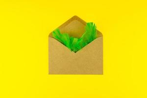 enveloppe artisanale en papier avec des plumes vertes sur fond jaune vif. concept créatif festif photo